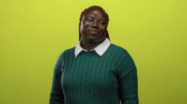 İzole edilmiş sarı bir arka plana gülümseyen, yeşil bir kazak giyen, hareketleriyle kendine güvenini ve güvenini ifade eden bir kadın..