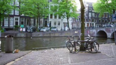 Yeşil yaprakların altında bisiklet, ağaç ve tarihi binaların bulunduğu Amsterdam Kanalı 'nın bulanık görüntüsü, sakin bir Avrupa kentsel manzarası sergiliyor.