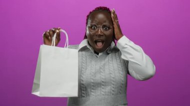 Beyaz bir alışveriş torbasını canlı pembe bir arka plana karşı tutarak neşeli duygular ve şık bir görünüm sergileyen bir kadın şaşkınlığını dile getiriyor..