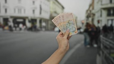Romen lei banknotlarını elinde tutan adam şehir sokaklarında, şehir içi halk ve binalara karşı para gösteriyor..
