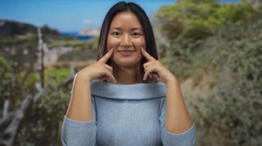 Güneşli bir parkta mavi bir süveter içinde gülümseyen bir kadın canlı mizaç ve gençlik cazibesini sergiliyor..