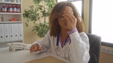 Steteskoplu doktor gözlüğü çıkarır ve baş ağrısına karşı klinik masasında tutar. Stres yorgunluğu..
