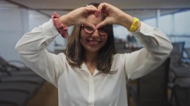 Teknede gülümseyen bir kadın elleriyle kalp şekli oluşturuyor. Mutluluğunu ve neşesini deniz kenarındaki bir arka planda sergiliyor. Açık havada sıcaklık ve pozitif titreşimleri ifade ediyor..