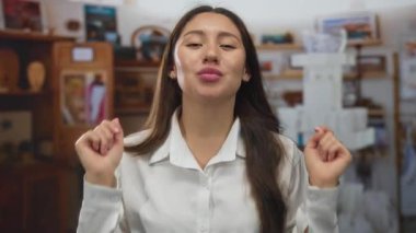 İki eli havada ve stüdyoda doğrudan göz teması kurarak öpüşme jesti için dudaklarını büzen bir kadın..