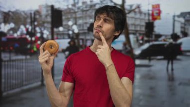 Yağmurlu caddede çenesinde parmak olan kırmızı tişörtlü bir adam, düşünceli sessiz tefekkür..