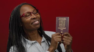 Kırmızı arka plan sergilenen seyahat belgelerine karşı elinde Czech pasaportu olan gülümseyen kadın.
