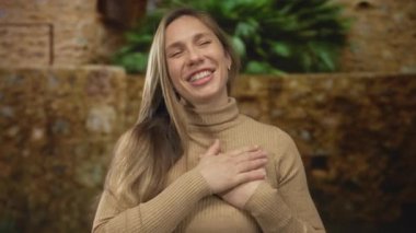 Kadın açık havada elleri göğsünde doğal bir taş ve yeşil yapraklı arka planda mutluluğu ifade ediyor. Huzurlu bir minnettarlık ve sıcaklık gösteriyor..