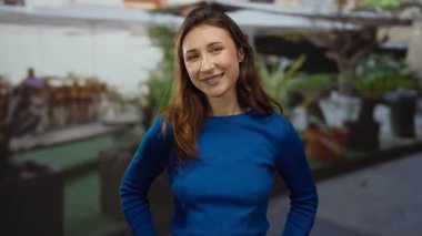 Şehir sokaklarında rahat bir çevrede günlük mavi elbiseli bir kadın gülümsüyor..