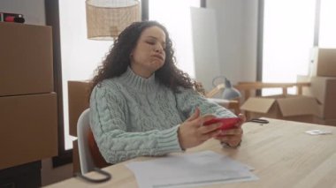 Yeni dairede bavulları boşaltan kadın etrafı kutularla çevrili ahşap masadaki telefonu kontrol ederek hareket sürecini ve modern yaşam alanına uyum sağlama sürecini gösteren evrakları hazırlıyor..