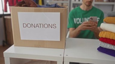 Adam bağış merkezindeki bağış masasında üzerinde bağış etiketi ve renkli süveter yığını olan büyük bir karton kutuyla akıllı telefonu kulağına tutuyor..