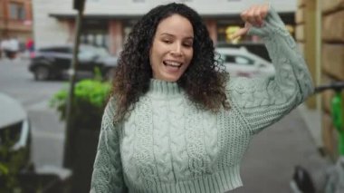 Gündüz vakti gülümseyen ve rahat süveter giyen bir kadın şehir caddesinde ayakta duruyor..