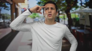 Akıllı gözlüklü bir adam, alnına yumruk indiriyor ve sokakta parlak güneş ışığı altında gözlerini kısıyor..