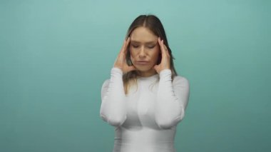 Beyaz gömlekli bir kadın, yeşil arka plana karşı elleri tapınaklarda, stres ve düşüncelerini ifade ediyor..