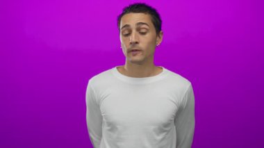 Düşünceli bir ifadeye sahip genç adam canlı pembe bir arka plana karşı duruyor, günlük beyaz bir gömlek giyiyor, izole edilmiş ve canlı bir stüdyo portresi yaratıyor..