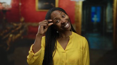 Müzede gülümseyen kıvırcık saçlı bir kadın canlı bir galeride jest yapıyor. Kültürel ifadeleri ve pozitifliği yansıtıyor..