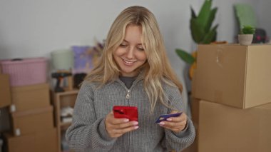 Yeni dairede akıllı telefon ve kredi kartı kullanan ve modern yaşam tarzını ve taşınma deneyimini gösteren kutuları olan bir kadın..