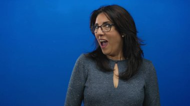 Mavi stüdyoda ağzı açık, elleri yanaklarında orta yaşlı bir kadın jest yapıyor. Sürpriz..