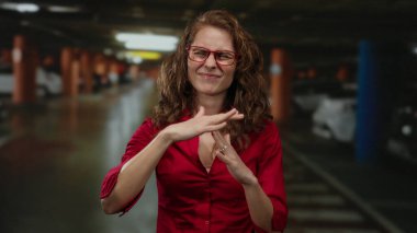 Kapalı otoparkta mola veren genç, kıvırcık saçlı ve gözlüklü bir kadın..