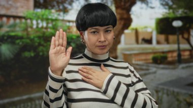 Parkta bağlılık yemini eden bir kadın çizgili bir kazak giyiyor, yeşilliklerle çevrili, içtenlik ve açık hava sükuneti duygusu taşıyor..