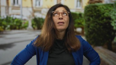 Orta yaşlı İspanyol kadın güneşli şehir sokağında alnı ağrılı, stres yorgunluğu baş ağrısı.