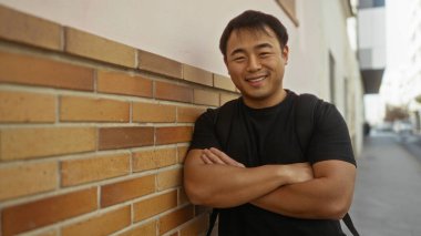 Kentin tuğla duvarına karşı duran genç adam gündelik şehir ortamını ve kendine güveni sergiliyor..