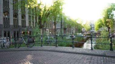 Köprü boyunca park etmiş geleneksel binalar ve bisikletlerle çevrili, güneş ışığının suya yansıdığı bulanık kanallar..