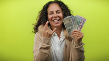 Orta yaşlı bir kadın elinde Hint rupisi notları tutarak parlak sarı bir zemin üzerinde kaya jestleri yaparak heyecan ve refahı ifade ediyor..