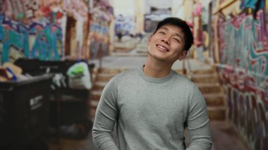 Şehrin renkli bir sokak yolunda mutlu bir şekilde gülümseyen genç adam, dinamik bir şehir manzarasında neşe ve günlük giysiler sergiliyor..