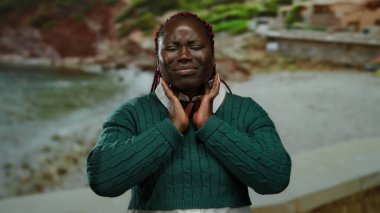 Deniz kenarında boynu ağrıyan yeşil kazak giyen bir kadın okyanus manzaralı ve doğal manzaralı manzaralı sahilin ortasında rahatsızlık veriyor..