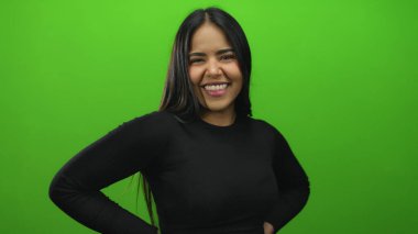 Uzun saçlı, parlak yeşil arka planda, duvarın üzerinden izole edilmiş siyah kıyafetli, kendine güvenen genç bir kadın pozitiflik ve çeşitliliği gösteriyor..