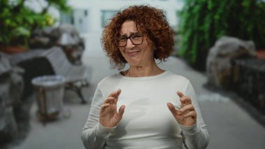 Kıvırcık esmer saçlı İspanyol kadın yeşil ve kentsel unsurlarla çevrili bir şehir caddesinde duygularını ve dışavurumunu tasvip etmiyor..