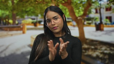 Parkta el çırpan elleri olan bir kadın, genç Latin kökenli ve açık havada yeşil ağaçların arasında, sıkılmış görünüyor..