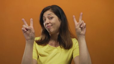 Latin kökenli orta yaşlı bir kadın tırnak işareti yapıyor ve stüdyoda hafif bir sırıtış sergiliyor..