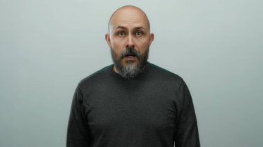 Kel sakallı, beyaz yüzlü beyaz bir adam kameraya bakarken beyaz arka planda siyah bir kazak giyiyor..