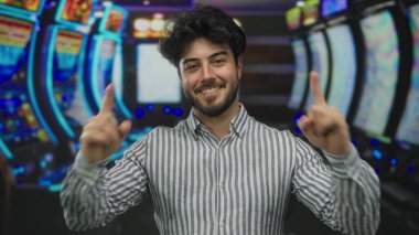 Sakallı genç adam arka planda renkli kumar makineleri olan canlı kumarhane ortamında eğleniyor..