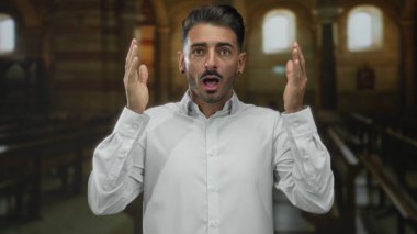 Kaldırılmış elleri, sıkılmış yumrukları ve kilisenin içinde ağzı açık, kemerli pencerelerin altındaki ahşap sıraların arasında duran adam; sürpriz.