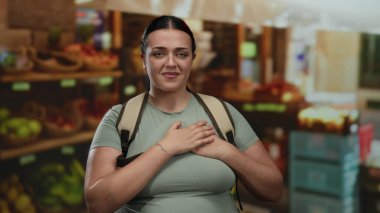 Kadın açık hava meyve pazarında rahat hissetmiyor. Renkli ürünleri ve canlı ortamları vurguluyor. Sırt çantası ve günlük giysiler giyip şehir keşiflerini resmediyor..