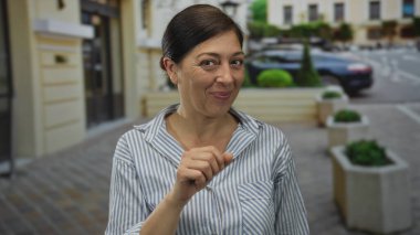 Bir kaldırım taşı caddesinde bir binanın girişinde elini tıklatarak gülümseyen bir kadın; dostça selamlaşma.