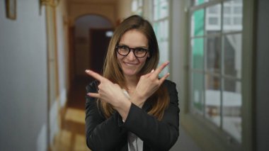 Genç bir kadın dilini uzatır ve parlak bir otel koridorunda kaya boynuzları hareketi yapar. Enerji heyecanı..