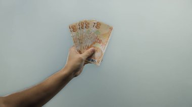 İzole edilmiş beyaz bir zemin karşısında elinde Türk lirası banknotları tutan adam, mali kavramları ve bölgesel ekonomiyi sembolize ediyor.