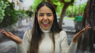 Çevresi doğa ve kentsel unsurlarla çevrili canlı bir sokakta neşeyle gülümseyen genç İspanyol kadın mutluluk ve enerji sergiliyor..