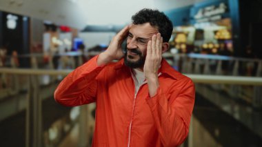 Portakal rengi tulumlu İspanyol adam arka planı bulanık, hareketli alışveriş merkezinde kafası karışmış görünüyor..