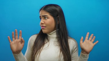 Mavi arka plan duvarı üzerinde beyaz kazak giyen bir kadın açık elle belirsizlik gösteriyor..