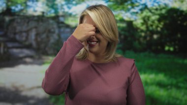 Mor süveter giyen kadın, yeşil çimenli güneş parkı yolunda burnunu çimdiklerken yüzünü buruşturuyor..