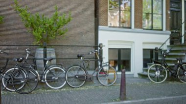 Bulanık bisikletler, arka planda tuğla ve pencerelerle Avrupa şehir caddesi boyunca dizilmiş güneşli bir günde açık, kentsel ve çözülmüş bir sahneyi yakalıyorlar..