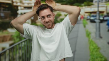 Sakallı genç adam gün ışığında şehir sokaklarında poz vererek eğleniyor..