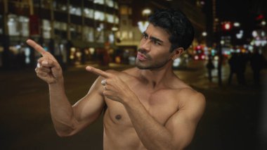 İspanyol gömleksiz adam çıplak göğsünü gösteriyor. Gece vakti neon ışıklı şehir caddesinde parmaklarını gösteriyor. Kararsızlık..