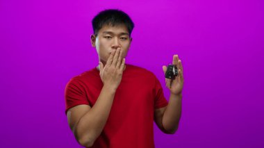 Kırmızı tişörtlü genç Çinli adam elinde araba anahtarlarıyla öpüşüyor. İzole edilmiş pembe arka plana karşı. Sevgi ve ulaşım taşıyor..