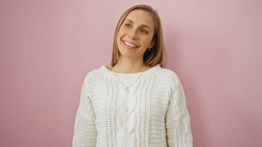 Pembe bir duvarın önünde gülümseyen bir kadın, örgü ören sıradan bir süveter tarzı sergiliyor. Sıcak ve pozitif bir ifade yayıyor..