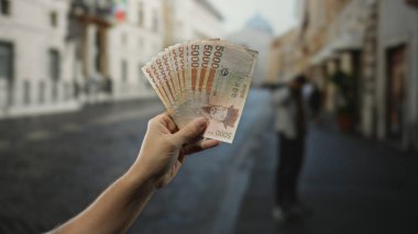 El ele tutuşan Güney Koreli şehir sokak ortamında arka planda bulanık bir adamla modern şehir ortamında para gösterisi yaparak kazandı..